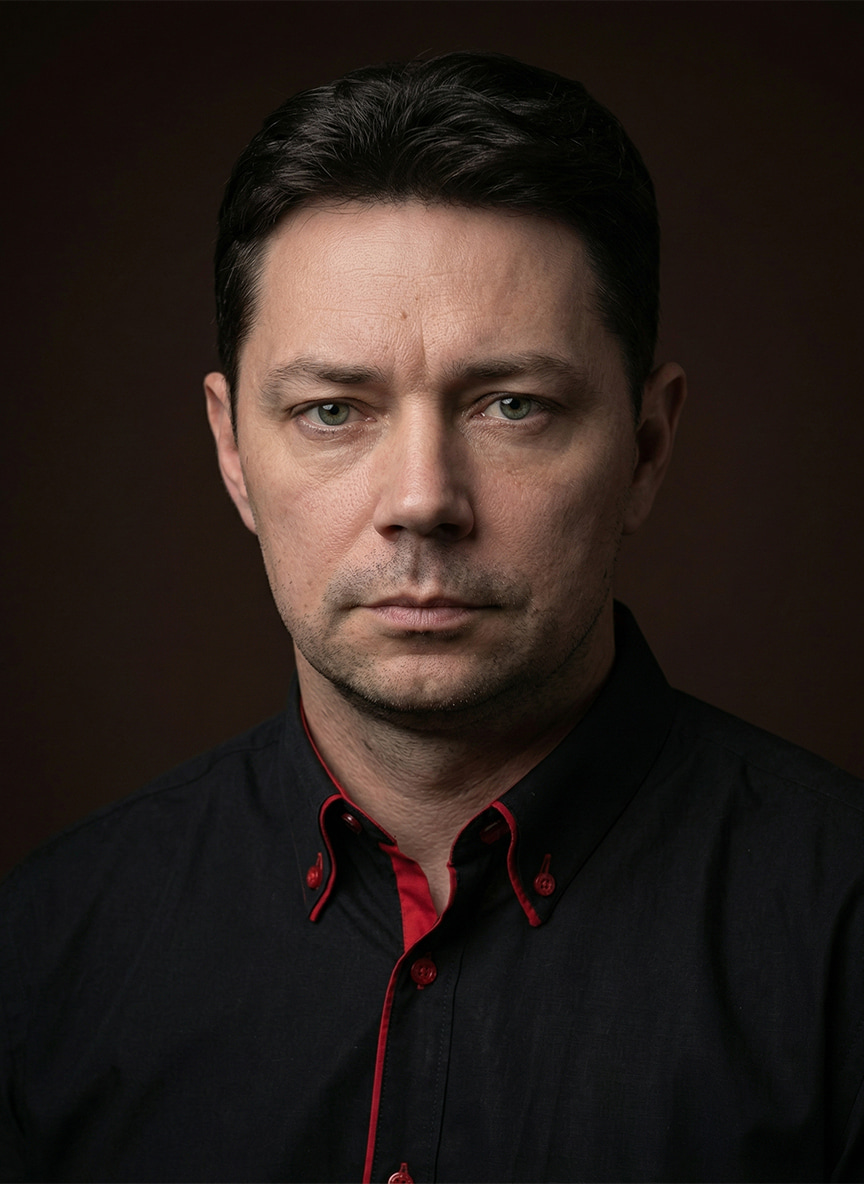 Portret dojrzałego mężczyzny z&nbsp;krótkimi, ciemnymi włosami, ubranego w&nbsp;czarną koszulę z&nbsp;czerwonymi akcentami na&nbsp;ciemnym tle. Prezentacja naturalnego efektu męskiego systemu uzupełniania włosów Hair Again.