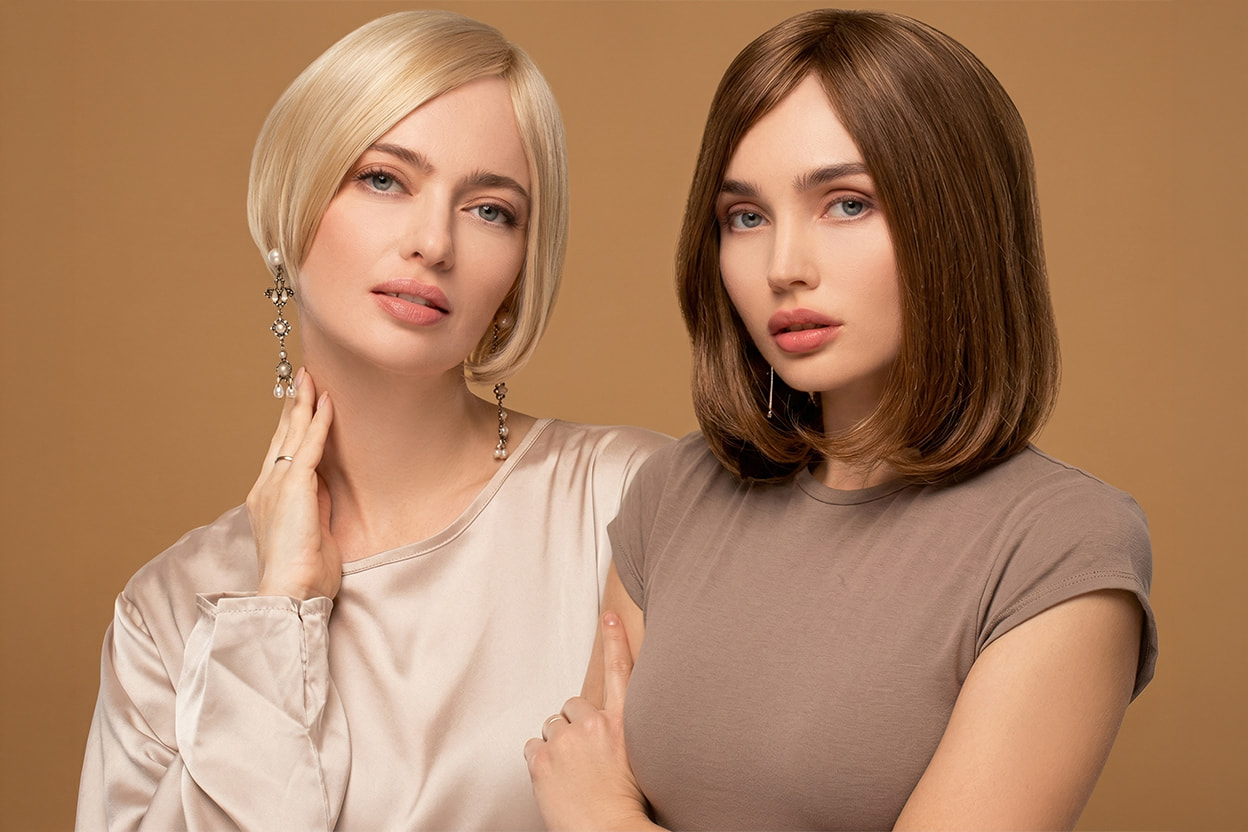Dwie kobiety prezentujące peruki naturalne z&nbsp;oferty Rokoko. Z&nbsp;lewej strony krótka peruka blond w&nbsp;stylu bob, z&nbsp;prawej klasyczna peruka brązowa do&nbsp;ramion na&nbsp;beżowym tle.