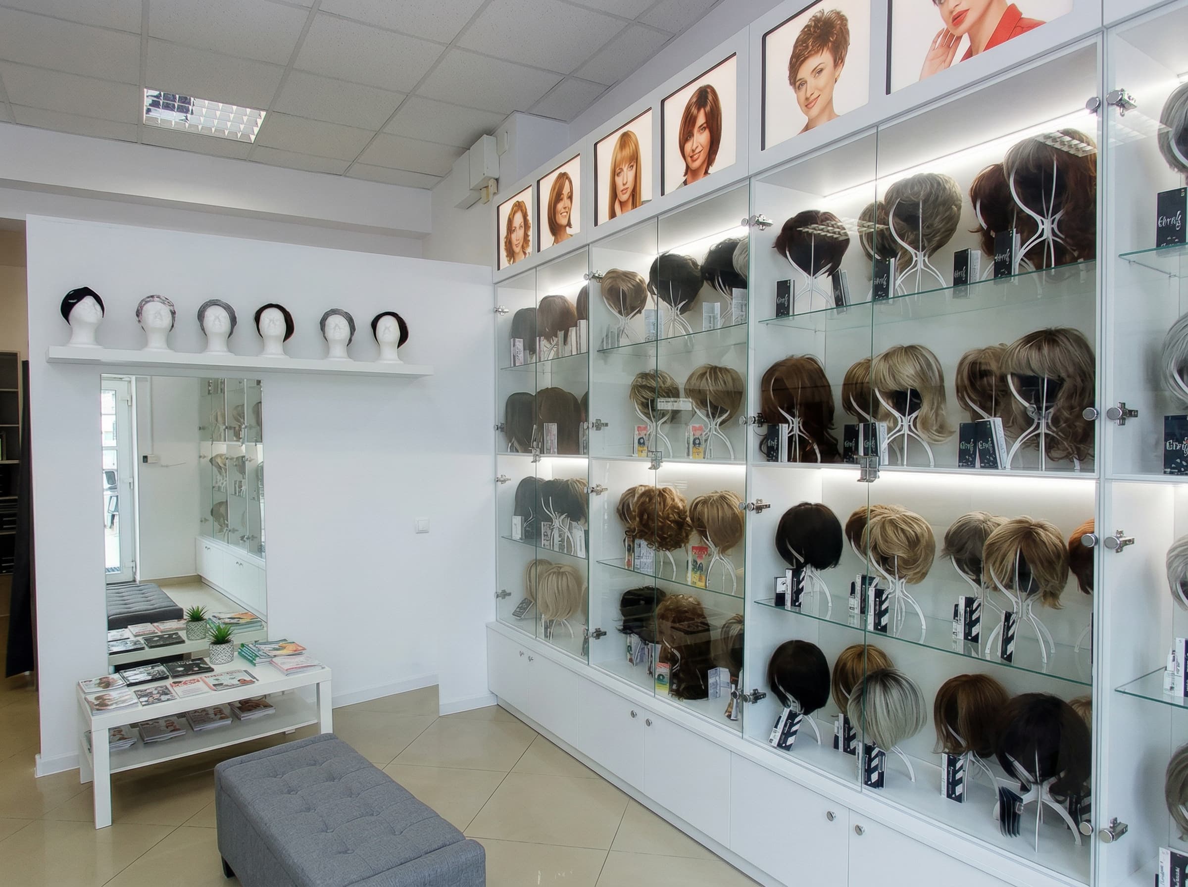 Jasne, nowoczesne wnętrze salonu Rokoko w&nbsp;Bydgoszczy z&nbsp;podświetlanymi gablotami, na&nbsp;których eksponowane są peruki na&nbsp;głowach manekina.