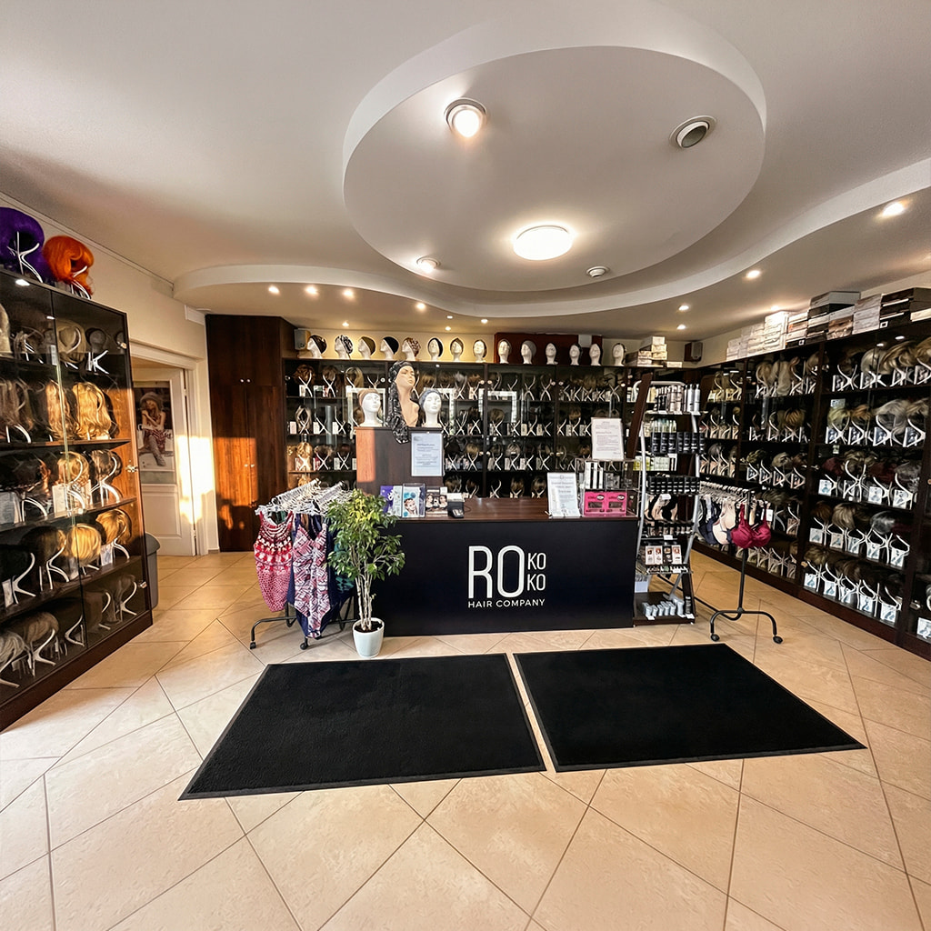 Jasne, nowoczesne wnętrze salonu peruk Rokoko na&nbsp;warszawskim Ursynowie z&nbsp;podświetlanymi gablotami pełnymi peruk na&nbsp;manekinach.